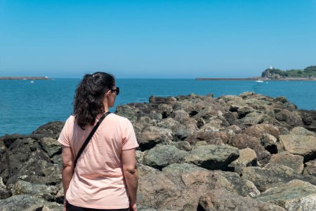 Tourist woman in front of a stone fortification in the sea while enjoying the landscape in Saint Jean de Luz, in the Basque Country in France