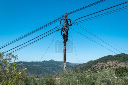 Wooden pole with many telephone cables in contrast to the blue sky and with large mountains in the background covered by forest