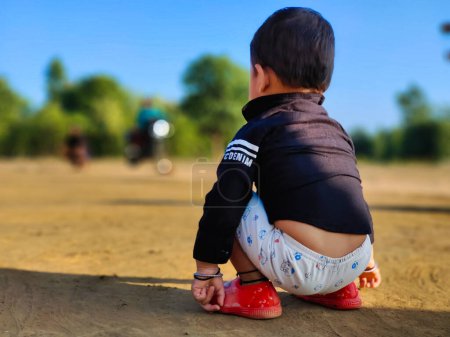 Photo for Cute little baby boy sitting in a park and smiling. Child crawling in a public park and looking forward. View from back. Copy space for text - Royalty Free Image