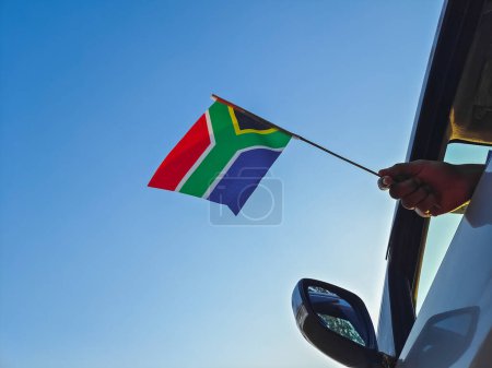 Boy waving South Africa flag against the blue sky from the car window close-up shot. Man hand holding South African flag, Copy space 