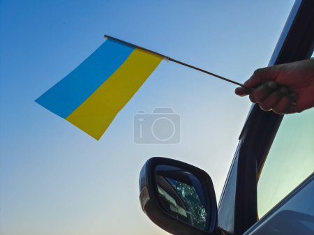 Foto de Boy waving Ukraine flag against the blue sky from the car window close-up shot. Man hand holding Ukrainian flag, Copy space - Imagen libre de derechos