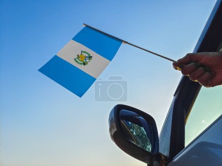 Foto de Boy waving Guatemala flag against the blue sky from the car window close-up shot. Man hand holding Guatemalan flag, Copy space - Imagen libre de derechos