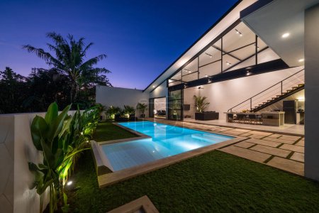 Téléchargez les photos : Villa tropicale vue avec jardin, piscine et salon ouvert au coucher du soleil. - en image libre de droit