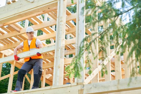 Photo for Front view of worker, craftsman standing, carrying, holding, putting wooden gilder outdoors. Builder wearing yellow vest and white helmet, constructing. Concept of building. - Royalty Free Image