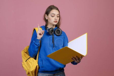 Front view of pretty schoolgirl wearing blue khudi and jeans, reading. Young female student holding open folder, raising finger, showing attention. Concept of student life.