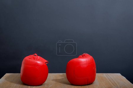 Photo for A beautiful set of two red lady's leather boxing gloves are on the light wooden table near a dark grey wall as a background, ready for competition for weekend activity. Studio photo. - Royalty Free Image