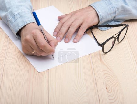 Photo for The hands of a man dressed on blue office t-shirt with classic wrist watch and golden ring on his hands, draws using red pencil a chart of rising stock prices on the rustic wooden structure table. - Royalty Free Image