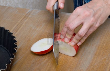 Eine weißhäutige Frau beim Zubereiten von Apfelkuchen in ihrer heimischen Küche. Nahaufnahme der Hände beim Schneiden reifer Äpfel.