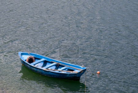 A blue colored wooden boat floats on the water in windy sunny weather. Top view of an old wooden boat without oars.
