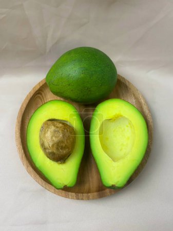 Foto de Aguacates enteros y divididos en un plato de madera. Concepto de alimentos saludables para frutas. - Imagen libre de derechos