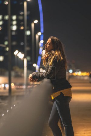 Téléchargez les photos : Femme seule posant et réfléchie regardant nulle part éclairée par une bougie de la ville avec un fond flou - en image libre de droit