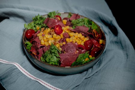 Photo for Cold cut beef meat sliced in light summer salad with greens, lettuce, sweet corn, cherry tomatoes, french baguette, deli meat  as luncheon snack or dinner dark background - Royalty Free Image