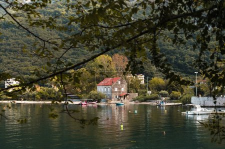 Foto de Paisaje otoñal en montenegro, cielo nublado gris, montañas, casa de piedra, tejas rojas, final de temporada turística, gente nadando en el mar - Imagen libre de derechos