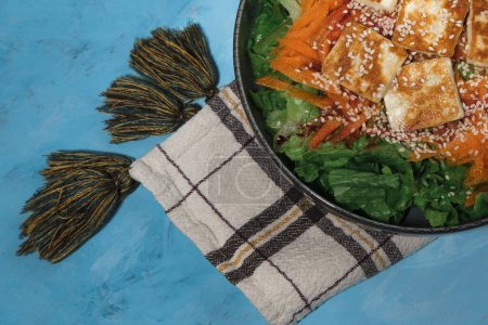 Foto de Ensalada verde con zanahoria y queso halloumi frito en sartén, servilleta textil de cocina, servida sobre fondo de textura azul - Imagen libre de derechos