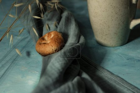 cup of tea or coffee hot beverage , bisquitte served on blue wooden background with kitchen textile cloth and dry plant as minimal decoration