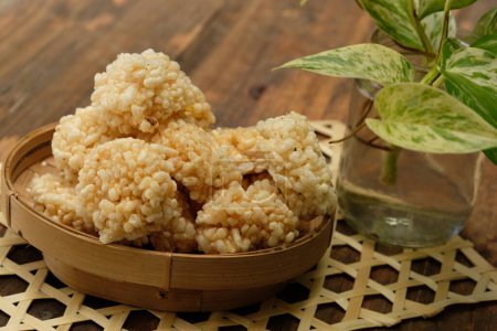 El rengginang es un aperitivo típico indonesio hecho de granos de arroz glutinoso que se sazonan y fríen. Se sirve en un recipiente de bambú sobre una mesa de madera. Comida indonesia. Camilan gurih.