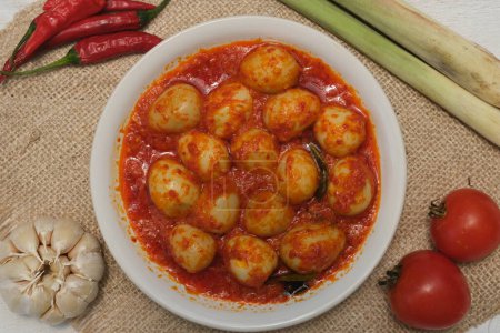 Foto de Telur Balado Tomate o Huevos Picantes comida tradicional indonesia popular hecha de huevos cocidos con pasta de tomate y chile o sambal, servido en plato de barro sobre mesa de madera. Ajo, tomate, chile. - Imagen libre de derechos