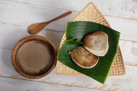 Photo for Serabi Surabi Kocor is traditional Javanese snacks made of rice flour, coconut milk, pandanus leaves, and palm sugar. Served in bamboo woven basket on wooden table. Flat lay. Indonesian food. - Royalty Free Image