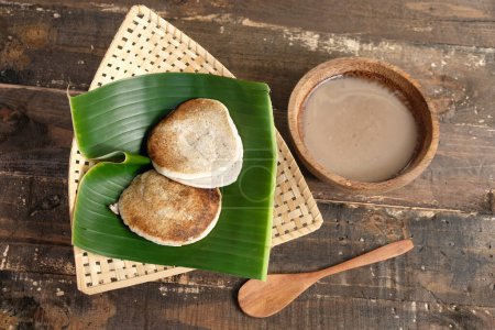 Photo for Serabi Surabi Kocor is traditional Javanese snacks made of rice flour, coconut milk, pandanus leaves, and palm sugar. Served in bamboo woven basket on wooden table. Flat lay. Indonesian food. - Royalty Free Image