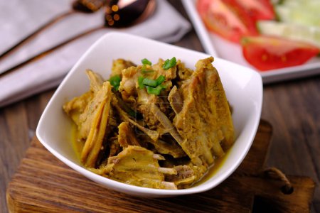 Photo for Tengkleng Kambing is a traditional Central Javanese dish made from young goat bones, with spices, soy sauce, chili. served in a white ceramic bowl on a brown wooden table. Indonesian food. - Royalty Free Image