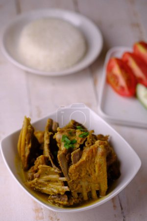 Photo for Tengkleng Kambing is a traditional Central Javanese dish made from young goat bones, with spices, soy sauce, chili. served in a white ceramic bowl on a brown wooden table. Indonesian food. - Royalty Free Image
