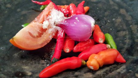 Foto de Close up of ingredients for making chili sauce on a clay plate. Red chili, green chili, tomato, onion, and salt. - Imagen libre de derechos