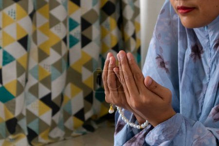 Eine muslimische Frau trägt muslimische Kleidung mit Hijab namens Mukena und hebt die Hände zum Gebet