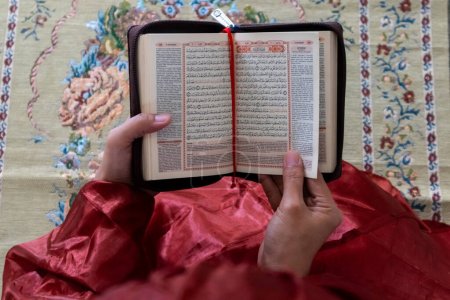 Hand of a Muslim woman holding the quran with Indonesian translation
