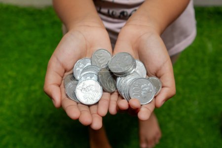Indonesische Münzen in Händen. Asiatisches Kind mit indonesischem Münzgeld. Geld sparen und Investitionskonzept.
