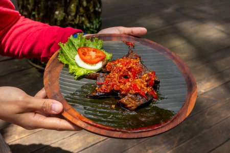 Téléchargez les photos : Mains tenant une assiette en bois de poumons frits de bœuf avec sauce rouge épicée ou Paru Goreng Balado - en image libre de droit