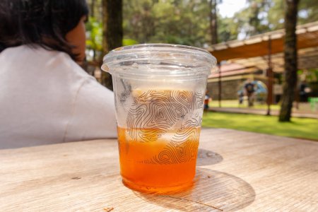Téléchargez les photos : Un thé glacé frais dans une tasse à emporter dans la table avec fond de nature - en image libre de droit