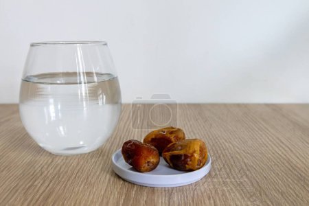 Ein kleiner Teller Dattelfrüchte und ein Glas Wasser auf einem Holztisch