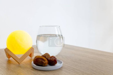 Ein kleiner Teller Dattelfrüchte auf einem Holztisch mit einem Glas Wasser und Lampe
