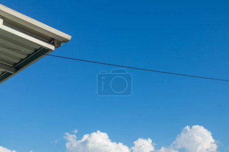 Téléchargez les photos : Vue du bord du toit métallique avec câble suspendu sur le toit résidentiel. Ciel bleu clair. - en image libre de droit