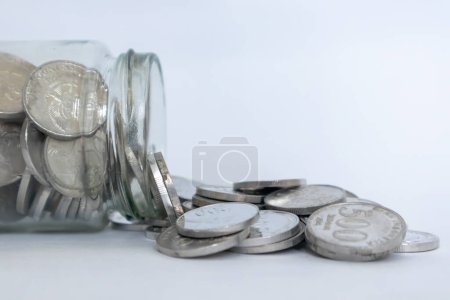 Glass jar of Indonesian Rupiah coins spilled on a white background. Coins in glass jar. Business and finance concept.