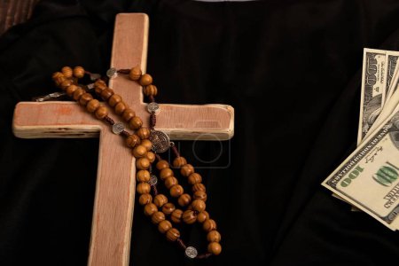 Téléchargez les photos : Une croix catholique, un chapelet avec des perles et des dollars reposent sur les vêtements noirs du prêtre avant le service dans le temple. - en image libre de droit