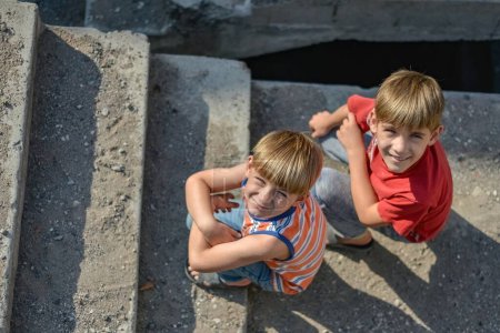 Téléchargez les photos : Deux enfants sont assis sur les marches d'un bâtiment abandonné, un concept de la vie des enfants de la rue orphelins
. - en image libre de droit