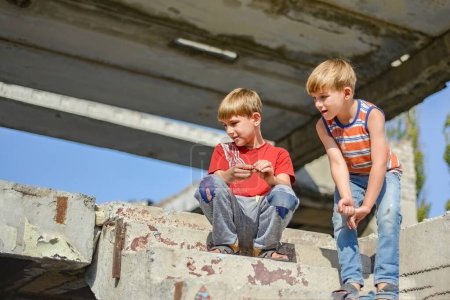 Téléchargez les photos : Deux enfants sont assis sur les marches d'un bâtiment abandonné, un concept de la vie des enfants de la rue orphelins
. - en image libre de droit