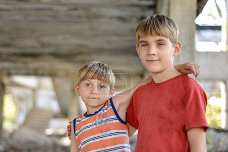 zwei Brüder stehen in einer Umarmung vor dem Hintergrund eines unvollendeten und verlassenen Gebäudes, ein Konzept für das Leben von Straßenkindern von Waisenkindern.