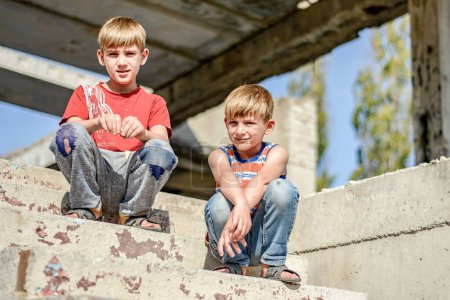 Foto de Dos niños están sentados en las escaleras de un edificio abandonado, un concepto de la vida de los niños huérfanos de la calle
. - Imagen libre de derechos