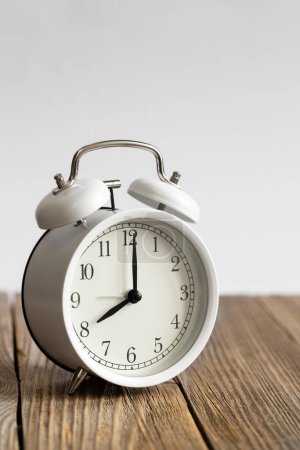 Foto de Reloj despertador blanco en una superficie de madera primer plano, fondo blanco borroso, espacio para el texto, concepto de mañana, plazo, gestión del tiempo. - Imagen libre de derechos