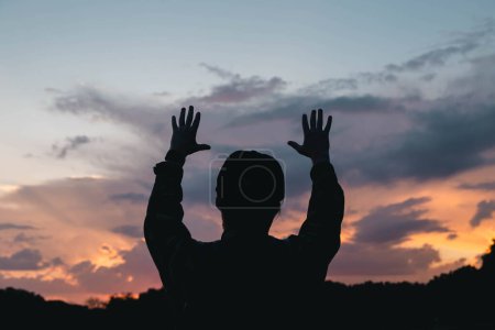 Photo for A young Christian man with a beard in nature raises his hands to the sky, thanks God, praises. - Royalty Free Image