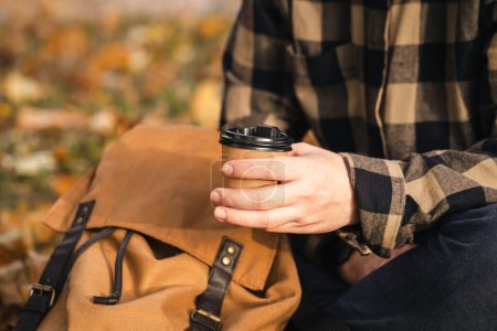 Foto de Una taza de papel de café en una mano de hombre en un parque de otoño, una bebida caliente para llevar con usted en la estación fría, un paseo por el bosque, espacio para copiar. - Imagen libre de derechos
