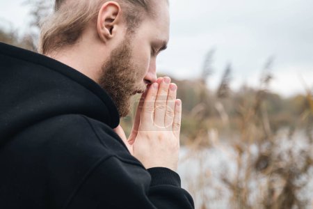 Photo for Young bearded Christian man praying in nature with his hands folded in prayer, copy space. - Royalty Free Image