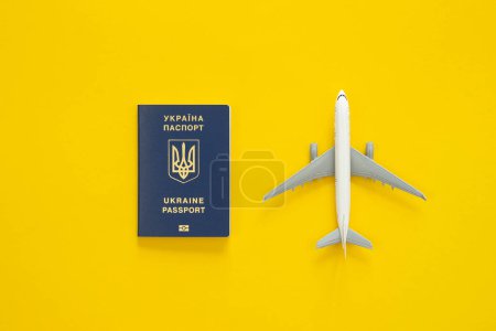 Photo for Ukrainian biometric passport, dollar bills and airplane figurine on a yellow background, top view. The concept of travel, migration and refugee from Ukraine. - Royalty Free Image