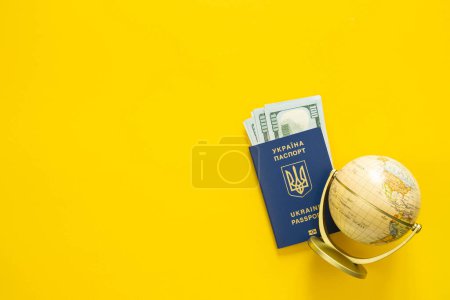 Photo for Biometric passport of a citizen of Ukraine, money and globe on a yellow background, top view. Ukrainian passport and money, travel concept. Copy space. - Royalty Free Image