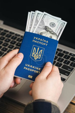 Photo for Ukrainian biometric passport and dollar bills in the hands of a man against the background of a laptop. - Royalty Free Image