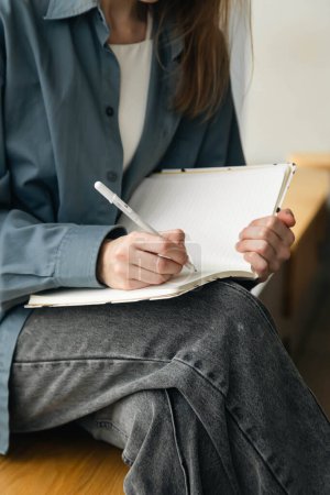 Close-up of a female hand writing on an blank notebook with a pen. A young woman student writes in a notepad.