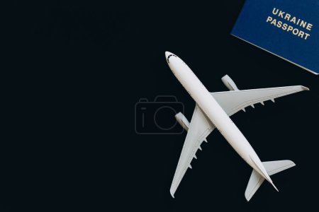Photo for Ukrainian biometric passport, dollar bills and airplane figurine on a black background, top view. The concept of travel, migration and refugee from Ukraine. - Royalty Free Image