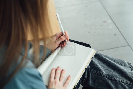 Gros plan des mains féminines tenant le stylo et écrivant dans un bloc-notes vide. Une jeune étudiante écrit dans un bloc-notes.